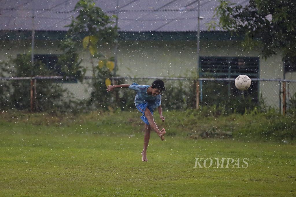 Anak bermain sepak bola di Lapangan Kostrad, Petukangan Utara, Jakarta, saat hujan deras, Senin (25/1/2021).  