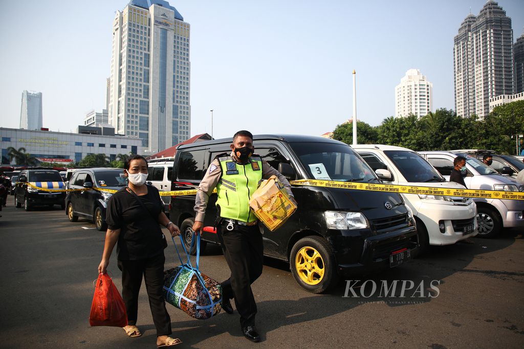 Petugas Polisi membantu membawa barang pemudik yang menjadi penumpang travel gelap yang terjaring operasi saat rilis di Polda Metro Jaya, Jakarta (29/4/2021). 