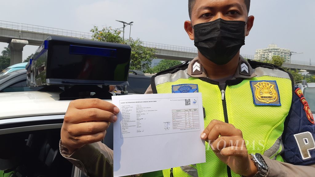 Seorang aparat polisi lalu lintas menunjukkan surat tanda lulus uji emisi usai mengikuti pengetesan pada kendaraan patrolinya di depan kantor Subdit Gakkum Ditlantas Polda Metro Jaya, Jakarta, Jumat (1/9/2023).