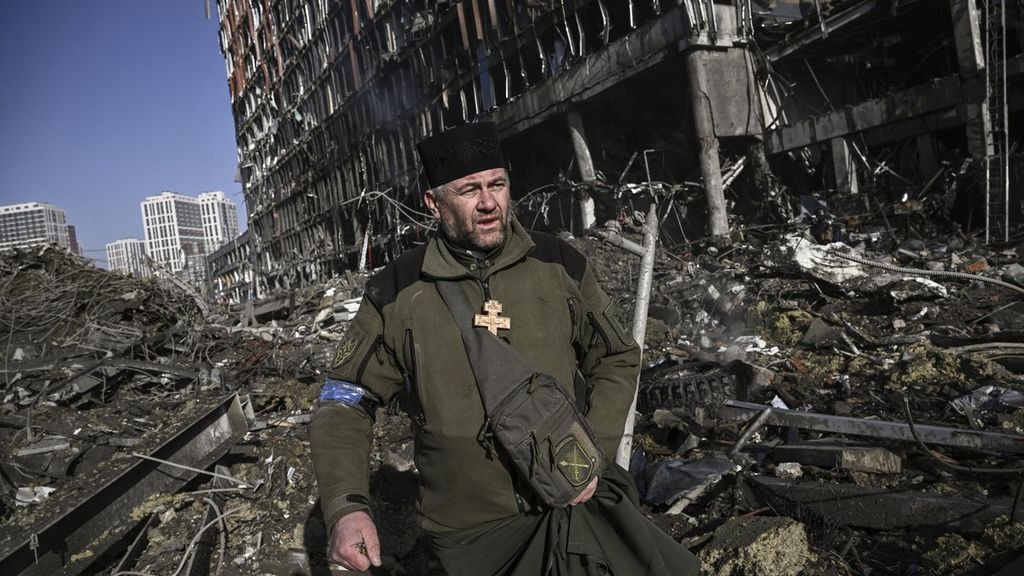 Pendeta tentara Ukraina Mikola Madenski berjalan melewati puing-puing di luar pusat perbelanjaan Retroville yang hancur di distrik perumahan setelah serangan Rusia di ibu kota Ukraina, Kiev, 21 Maret 2022.