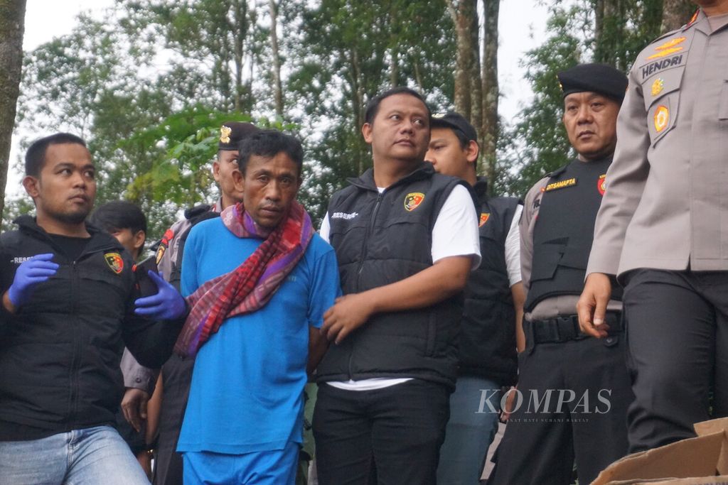 Slamet Tohari (center) is taken by a member of the Banjarnegara Police to a cassava plantation where the 12 victims he killed were buried in a case of doubling money in Balun Village, Wanayasa, Banjarnegara, Central Java, Tuesday (4/4/2023).