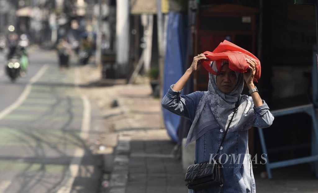 Warga menggunakan tas kain untuk melindungi kepala dari sengatan sinar matahari di daerah Tanah Abang, Jakarta Pusat, Senin (24/4/2023).