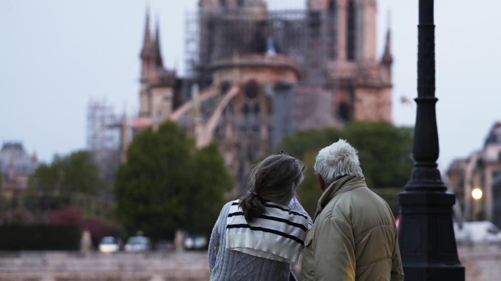 Sepasang suami istri melihat ke arah Katedral Notre-Dame di Paris, Perancis, saat petugas pemadam kebakaran terus berusaha memadamkan api, Selasa (16/4/2019).