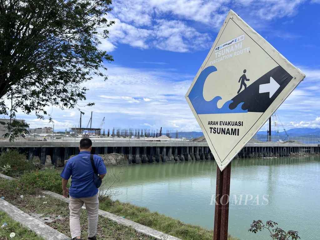 Warga melewati sebuah papan informasi yang dipasang di tepi jalan di pesisir Kabupaten Donggala, Sulawesi Tengah, Senin (27/3/2023).