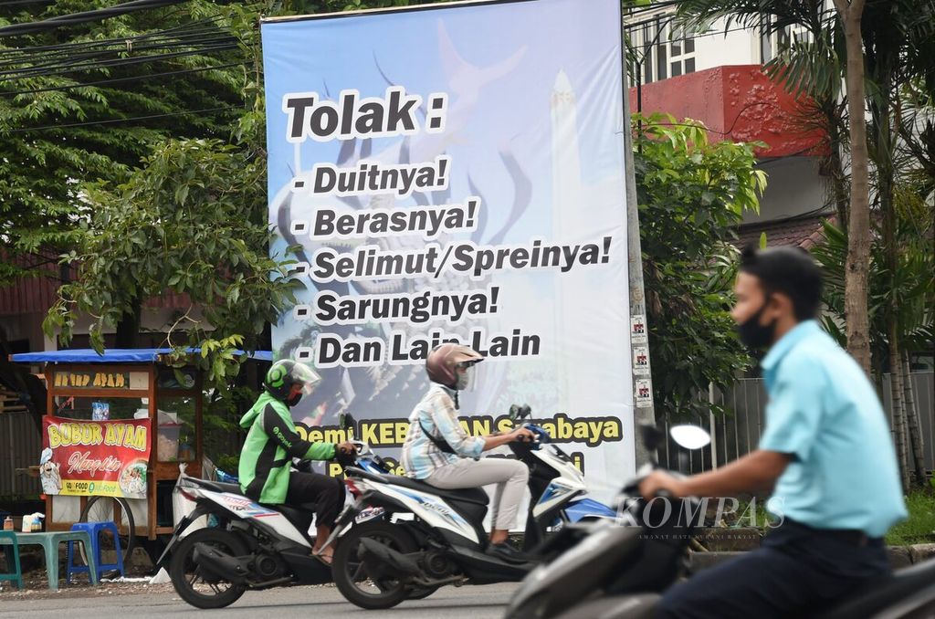 Warga melintas di depan spanduk anjuran untuk menolak pemberian dalam Pilkada Kota Surabaya di Jalan Kombes Pol M Duriyat, Surabaya, Jawa Timur, Senin (7/12/2020). 