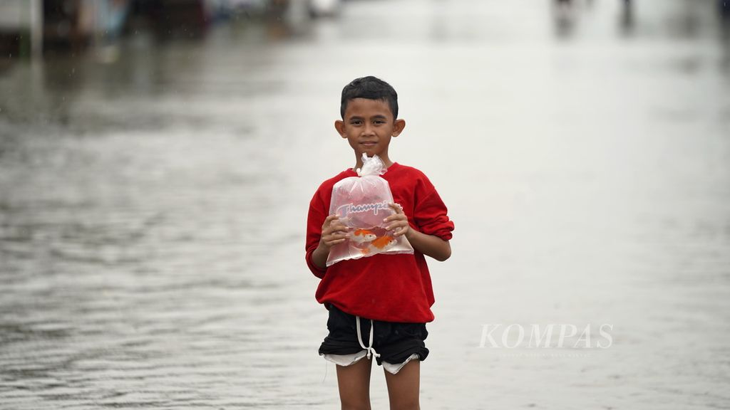 Seorang anak membawa ikan mas di antara air bah yang merendam Vila Kencana Cikarang di Desa Karangsentosa, Kecamatan Karangbahagia, Kabupaten Bekasi, Jawa Barat, Kamis (2/3/2023).