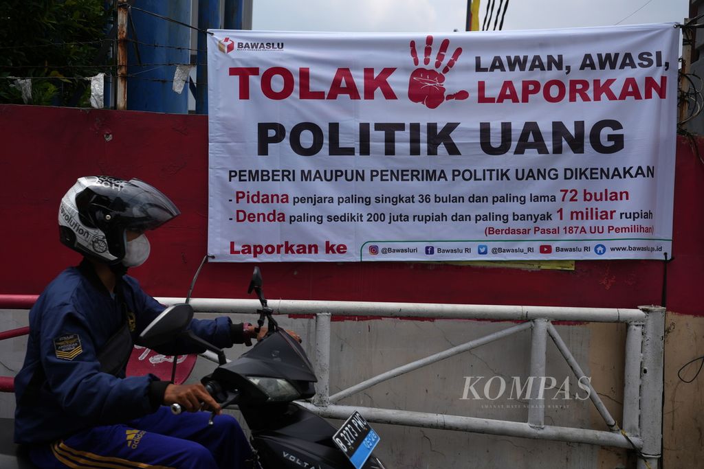 Warga melintasi baliho ajakan tolak politik uang dalam Pemilu 2024 yang dipasang oleh Bawaslu di Jalan Raya Margonda, Depok, Jawa Barat, Selasa (13/2/2024).