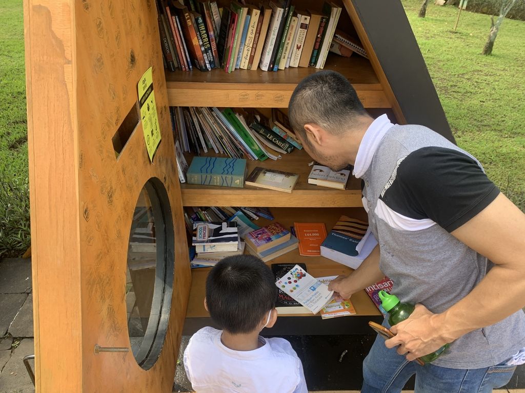 Pengunjung memanfaatkan rak buku milik Bookhive di Taman Menteng, Jakarta, Jumat (12/5/2023). Ruang baca dengan konsep perpustakaan bersama memperbolehkan pengunjung untuk meminjam dan menyimpan buku di rak milik Bookhive ini.