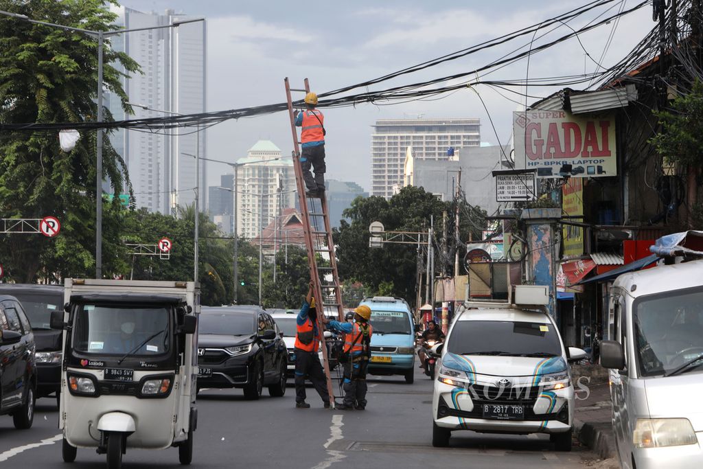 Petugas mengikat kabel yang melintang di atas pengendara di Jalan KH Mas Mansyur, Jakarta, Kamis (12/5/2022). Kabel-kabel yang melintang tersebut harus mendapat perawatan secara berkala agar tidak kendor sehingga tidak menganggu dan membayakan pengguna jalan.