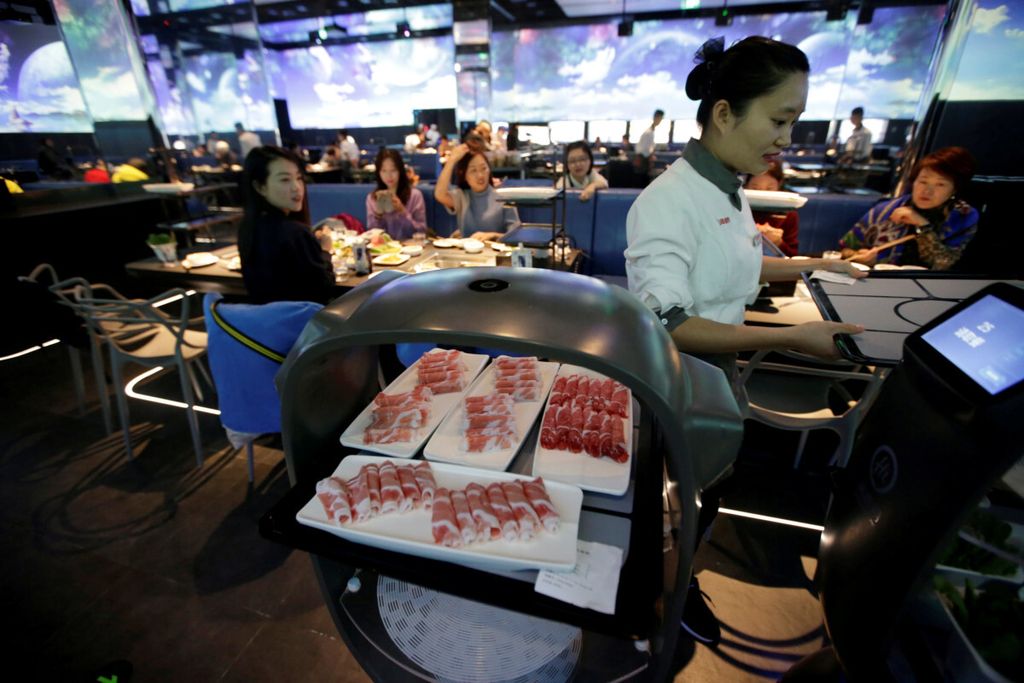 Robot pelayan membawa piring-piring makan malam yang dipesan tamu ke meja di restoran di Beijing, China, November 2018. 