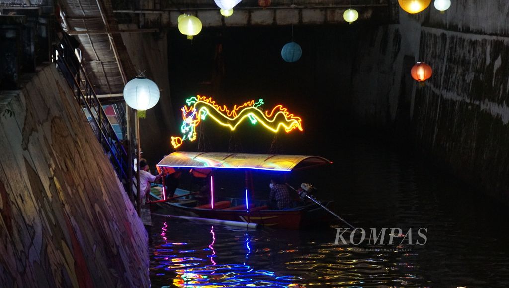 Perahu berhiaskan lampu warna-warni melintasi Kali Pepe dalam Grebeg Sudiro, di Kota Surakarta, Jawa Tengah, Senin (16/1/2023) malam. Keberadaan wisata perahu membangkitkan ingatan tentang kejayaan jalur transportasi air di kota tersebut pada masa lampau.