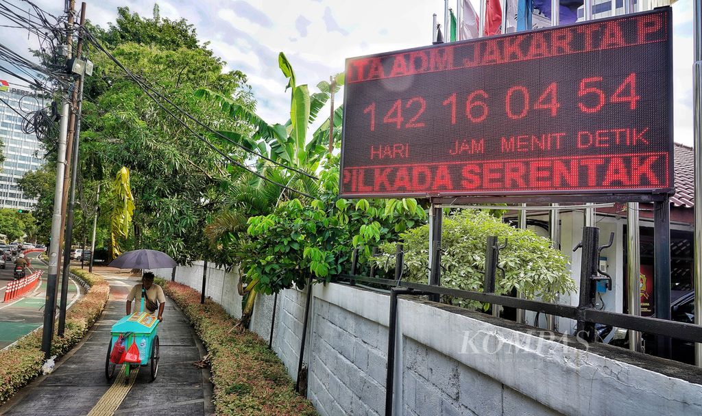 Seorang pedagang keliling melintas di dekat papan penghitung waktu menuju pelaksanaan Pilkada 2024 di depan Kantor Komisi Pemilihan Umum Jakarta Pusat, Jakarta, Minggu (7/7/2024).  