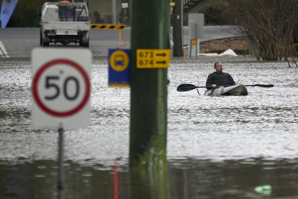 Seorang pria mendayung kayak melintasi jalan yang tergenang banjir di WIndsor, di pinggiran Sydney, Australia, 5 Juli 2022. 