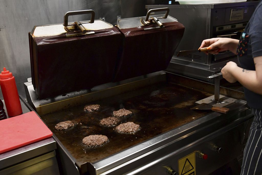 Seorang pekerja sedang menggoreng daging burger di Restoran Zing Burger di Budapest, Hongaria, Minggu (12/9/2022). Belanja energi listrik di negara ini mengalami kenaikan hingga 750 persen sepanjang tahun ini.
