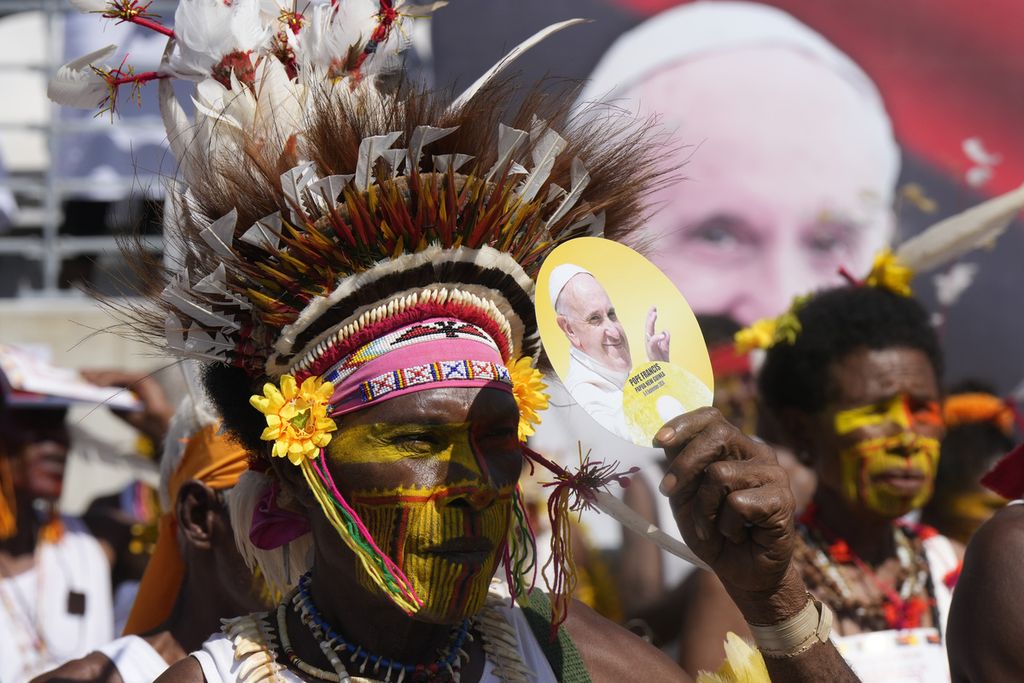 Seorang pria dengan hiasan kepala tradisional menggunakan kipas bergambar Paus Fransiskus untuk melindung wajah dari terik matahari saat Paus Fransiskus memimpin misa di Stadion Sir John Guise di Port Moresby, Papua Niugini, Minggu (8/9/2024). 