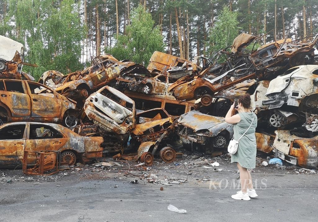 Warga berdiri di depan bangkai mobil yang ditumpuk di salah satu sudut kota Irpin, Provinsi Kyiv, Ukraina, Sabtu (18/6/2022). Mobil-mobil yang hancur akibat perang itu kini menjadi semacam ikon pertempuran antara Rusia-Ukraina di Irpin.