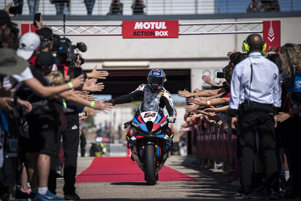 Pebalap tim Rokit BMW Mororrad, Toprak Razgatlioglu, disambut oleh tim dan para penggemarnya seusai finisi di posisi kedua dalam balapan dua Superbike di Sirkuit Aragon, Minggu (29/9/2024). Razgatlioglu berpeluang mengunci gelar juara dalam balapan di Estoril, 11-13 Oktober, jika meraih 23 poin lebih banyak dari Nicolo Bulega, dan tidak kehilangan poin lebih dari 19 poin dari Bautista.