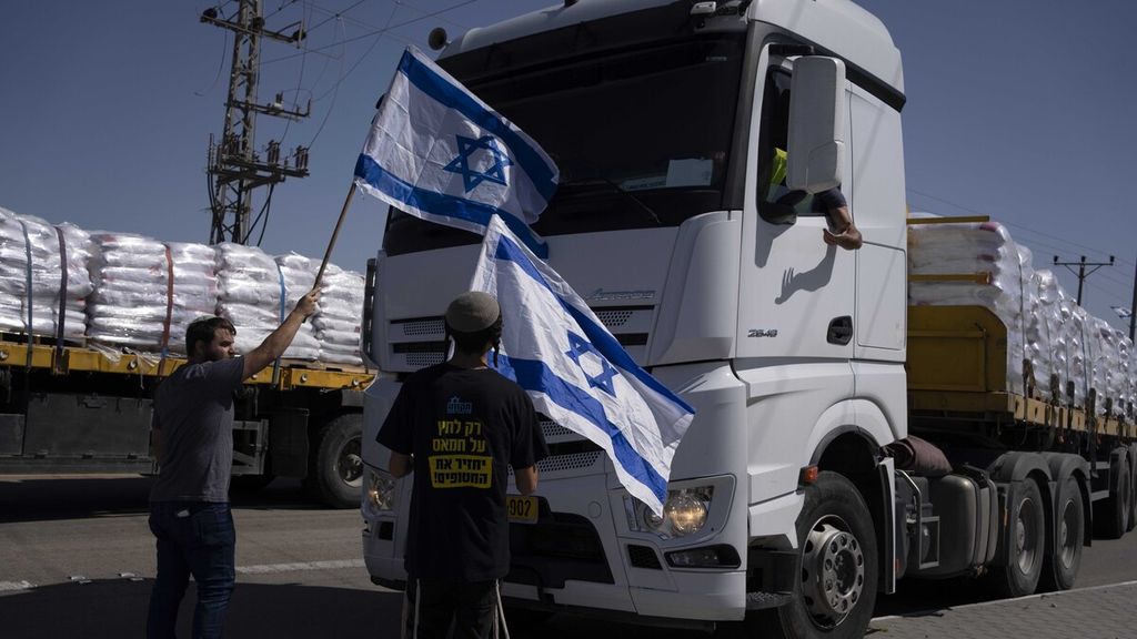 While holding the Israeli flag, people stand in front of a humanitarian aid truck entering the Gaza Strip near the Kerem Shalom border in southern Israel on May 9, 2024.
