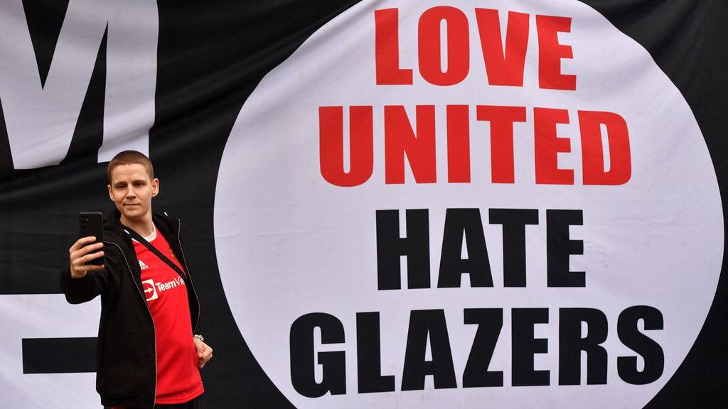 Seorang penggemar Manchester United tengah berswafoto di depan poster berisikan gerakan menentang keluarga Glazer, pemilik klub MU, 22 Agustus 2022 di depan Stadion Old Trafford, Manchester. 