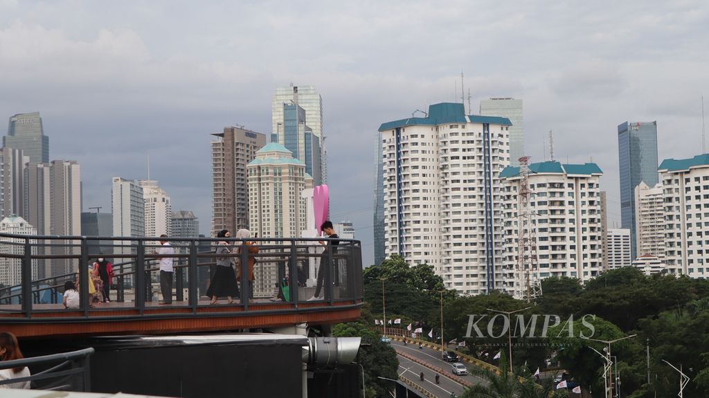 Warga menikmati pemandangan gedung tinggi di Jakarta dari jembatan Skywalk di atap gedung Mal Senayan Park, Jakarta Pusat, Rabu (8/2/2023).