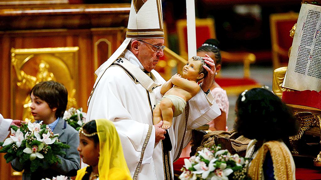 Paus Fransiskus  memegang sebuah patung bayi Yesus pada misa Natal di Basilika Santo Petrus di Vatikan, Minggu (24/12)  waktu setempat