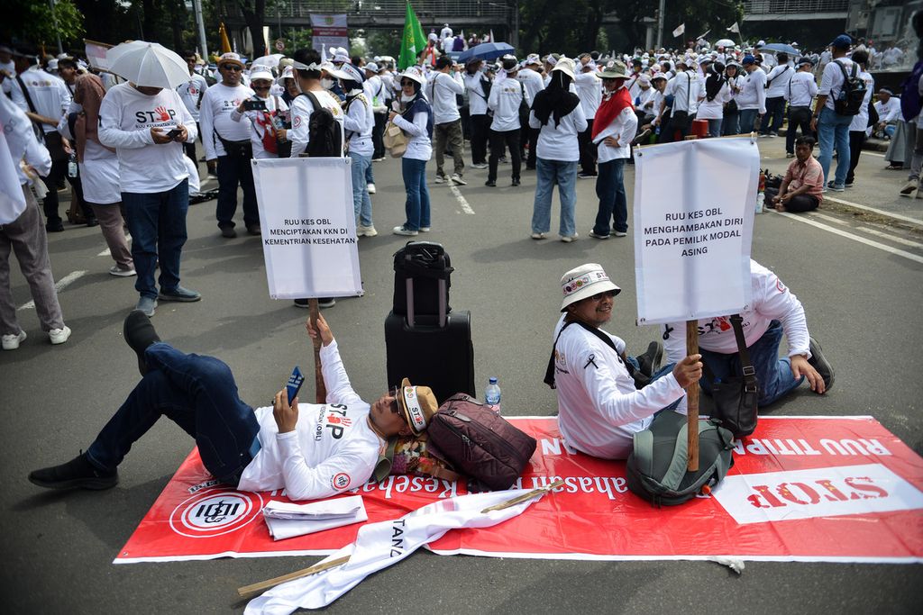 Dua peserta aksi mengangkat poster berisi pesan penolakan regulasi <i>omnibus law</i> atas Rancangan Undang-Undang (RUU) Kesehatan saat aksi di kawasan Patung Kuda Arjuna Wiwaha, Jakarta Pusat, Senin (8/5/2023). 