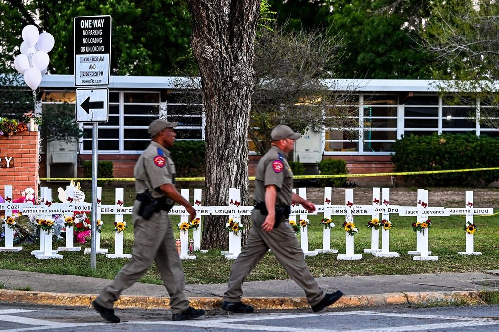 Petugas keamanan, Kamis (26/5/2022), melintas di titik peringatan sementara bagi korban penembakan di Sekolah Dasar Robb, di Uvalde, Texas, Amerika Serikat. Puluhan orang meninggal akibat penembakan yang dilakukan remaja di sekolah itu pada 25 Mei. 