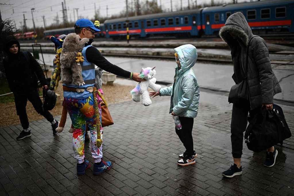 Seorang relawan dari Inggris, David Fricker (kedua dari kiri) menyerahkan boneka - dari ribuan mainan yang didonasikan oleh anak-anak Inggris melalui prakarsa Teddy Busz - pada seorang anak Ukraina yang tiba di Stasiun Zahony, perbatasan Ukraina-Hongaria pada Sabtu (9/4/2022) untuk mengungsi.