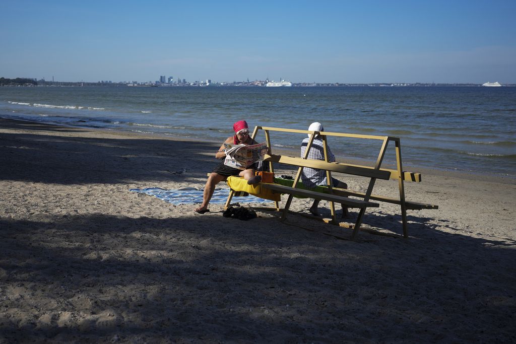 Seorang perempuan membaca koran di Pantai Pirita di Laut Baltik di Tallinn, Estonia, 5 Agustus 2022.