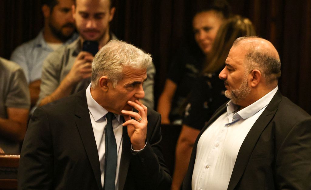Menteri Luar Negeri Israel Yair Lapid (kiri), Kamis (30/6/2022), berbincang dengan Ketua Partai Ra'am - Partai Arab, Mansour Abbas (kanan), di tengah pemungutan suara pembubaran parlemen Israel. Naftali Bennett akan menjabat sebagai perdana menteri hingga pemilu terselenggara pada 1 November 2022. 