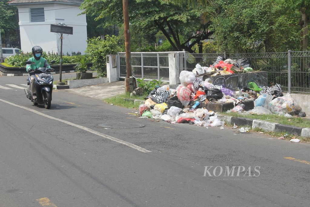 Residents crossing near a pile of overflowing garbage on the side of the road in Kotabaru Village, Gondokusuman District, Yogyakarta City on Monday (24/7/2023) afternoon. The garbage pile-up is a result of the closure of Piyungan landfill.