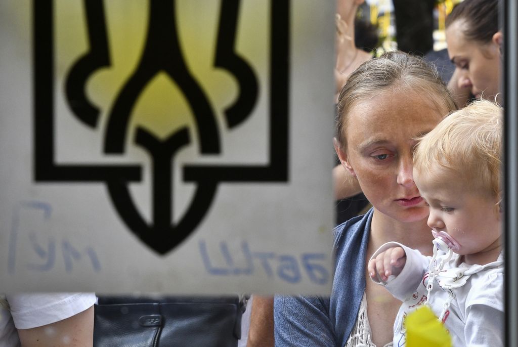 Alena dan putrinya, Sabina (2), pengungsi dari Melitopol, mengantre untuk mendapatkan jatah bantuan kemanusiaan di sebuah lokasi di Zaporizhia, Ukraina, Kamis (11/8/2022). Serangan roket pada hari yang sama di PLTN Zaporizhia oleh militer Rusia dan Ukraina menimbulkan kekhawatiran tentang potensi bencana nuklir yang bisa terjadi sewaktu-waktu. 
