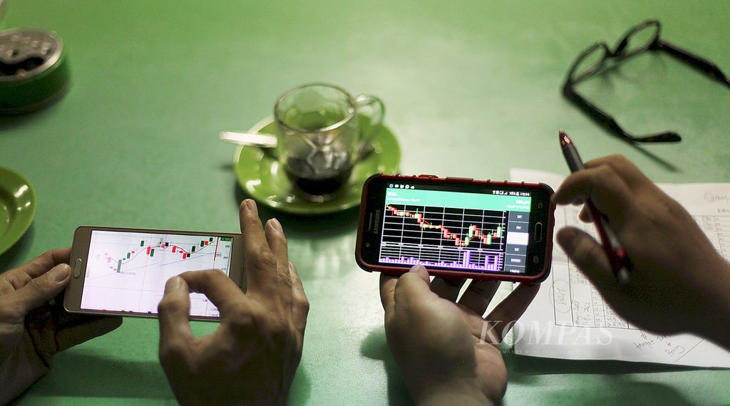 Karyawan percetakan di Jakarta, Rabu (19/10), memantau pergerakan saham melalui telepon pintar mereka di sela jam istirahat.
