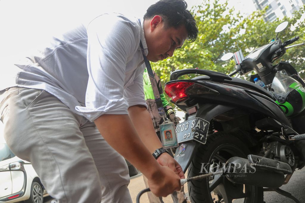 Petugas menguji emisi motor seorang pengendara ojek daring di parkiran Kantor Subdit Gakkum Ditlantas Polda Metro Jaya, Jakarta Selatan, Jumat (1/9/2023).