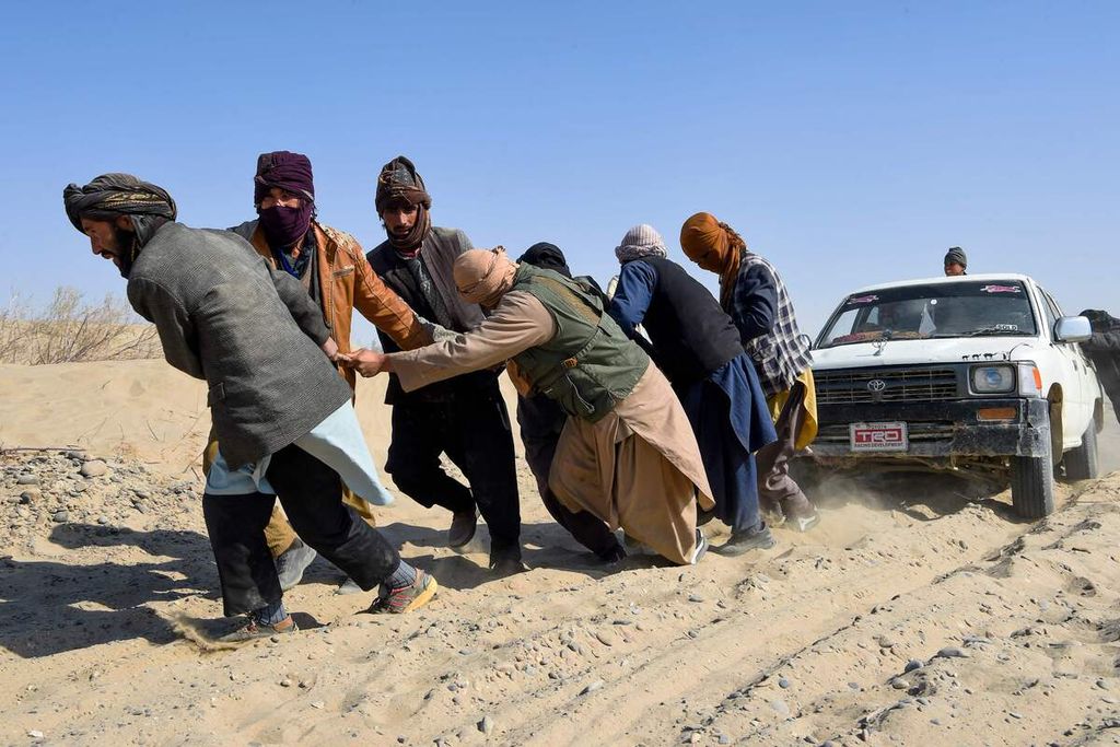 Dalam foto yang diambil pada 17 Februari 2022 ini tampak sejumlah imigran asal Afghanistan menarik pikc up yang terjebak di pasir di padang gurun yang tak jauh dari Nimruz, perbatasan Afghanistan-Iran.