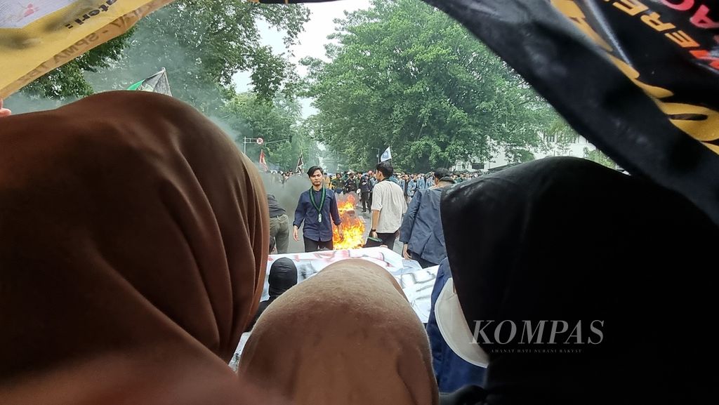 Sejumlah mahasiswa mendengarkan orasi sambil berteduh di bawah spanduk dalam unjuk rasa di Gedung Sate, Kota Bandung, Jawa Barat, Senin (11/4/2022).