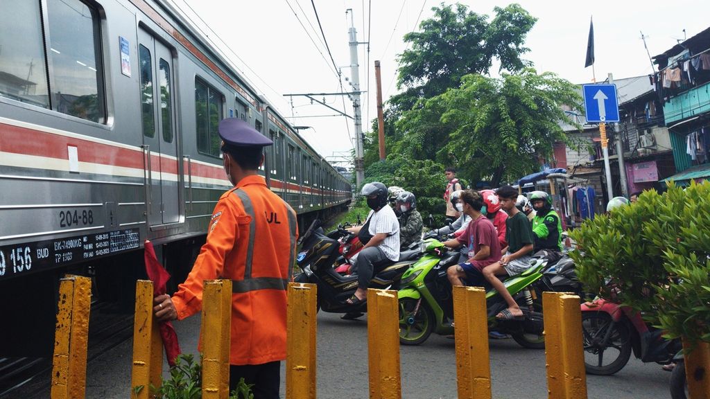 Seorang penjaga jalan lintasan kereta api mengatur lalu lintas saat kereta melintasi jalur di Jalan Jembatan Besi Raya, Kecamatan Tambora, Jakarta Barat, Rabu (8/2/2023).