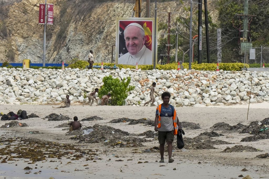 Warga setempat berjalan di sepanjang pantai dekat foto Paus Fransiskus menjelang kunjungan Paus ke Port Moresby, Papua Niugini, Kamis (5/9/2024).