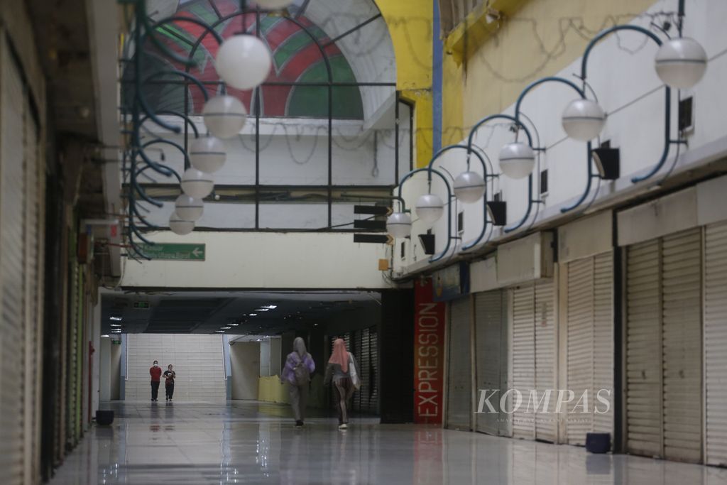Warga melintasi kios-kios yang mayoritas telah tutup di sepanjang lorong Mal Blok M, Jakarta Selatan, Minggu (29/1/2023). Walaupun pandemi bertahap berubah menjadi endemi, pusat perbelanjaan yang terkenal di awal tahun 2000-an ini saat ini seperti mati suri.