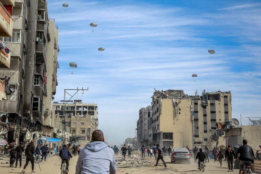 Warga Palestina berlarian mengejar bantuan kemanusiaan yang diterjunkan dengan parasut di kota Gaza, 1 Maret 2023. 