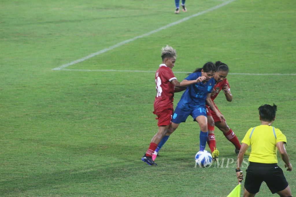 Pemain Thailand, Nacha Kaewanta (biru), diapit dua pemain Indonesia dalam pertandingan Semifinal Sepak Bola Putri AFF 2023 di Stadion Gelora Sriwijaya Jakabaring, Palembang, Sumatera Selatan, Kamis (13/7/2023). Dalam pertandingan tersebut, Indonesia kalah telak 1-7 dari Thailand.