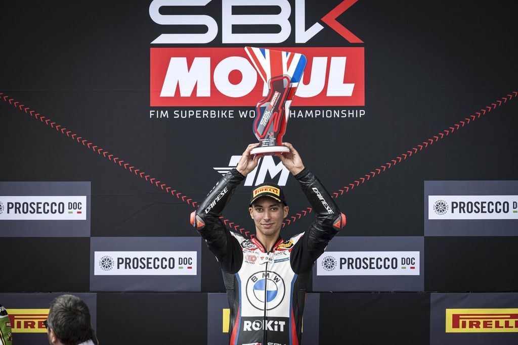 Pebalap tim Rokit BMW Motorrad WorldSBK, Toprak Razgatlioglu, mengangkat trofi seusai memenangi balapan 1 Superbike seri Inggris di Sirkuit Donington Park, Sabtu (13/7/2024). Razgatlioglu meraih tiga kemenangan di Donington Park, mengulang <i>hattrick </i>di Misano. Dia kini memuncaki klasemen dengan 241 poin.