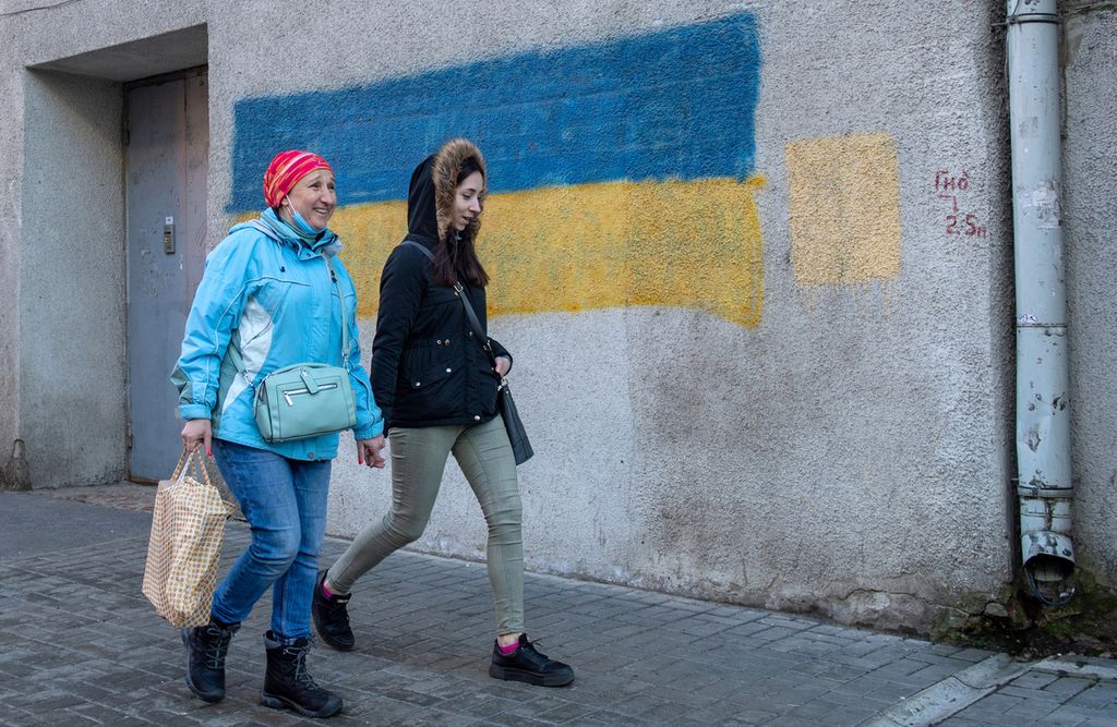 Dua wanita berjalan melewati bendera Ukraina yang dilukis di dinding di pusat kota terbesar kedua di Ukraina, Kharkiv, yang terletak sekitar 40 km dari perbatasan Ukraina-Rusia, Senin (21/2/2022). Ukraina pada 21 Februari 2022, mendesak pertemuan Dewan Keamanan PBB untuk mengatasi ancaman invasi Rusia.