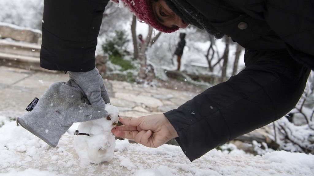 Seorang perempuan membuat manusia salju saat hujan salju di Athena, Senin (24/1/2022). Cuaca buruk telah melanda Yunani dengan suhu di bawah titik beku dan hujan salju di banyak bagian negara itu, termasuk ibu kota Athena, dan banyak negara lainnya.