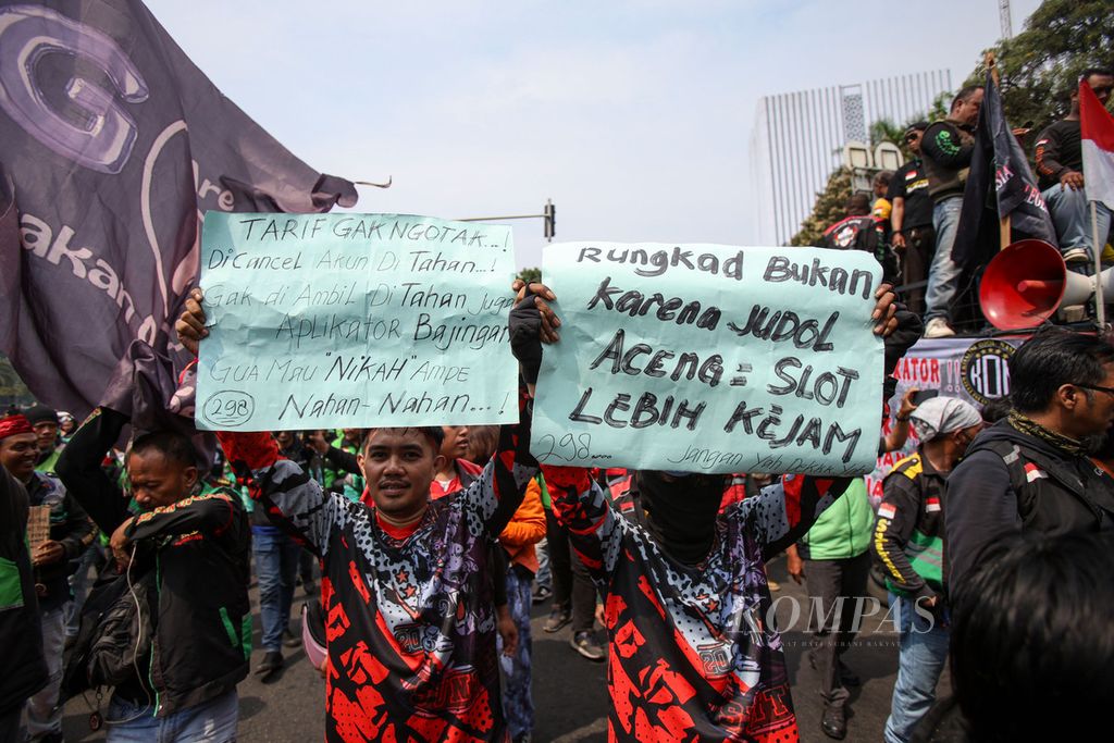 Dua pengemudi ojek <i>online</i> atau ojek daring membentangkan poster berisi tuntutan mereka saat melakukan unjuk rasa di kawasan Patung Kuda Wijaya, Jakarta, Kamis (29/8/2024).