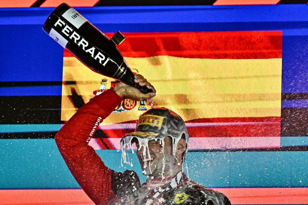 Pebalap Ferrari, Carlos Sainz Jr, menyiramkan sampanye ke kepalanya setelah memenangi balap Formula 1 seri Singapura di Sirkuit Jalan Raya Marina Bay, Singapura, Minggu (17/9/2023). Masa depan Sainz tidak jelas setelah kursinya di Ferrari bakal digusur oleh Lewis Hamilton. 