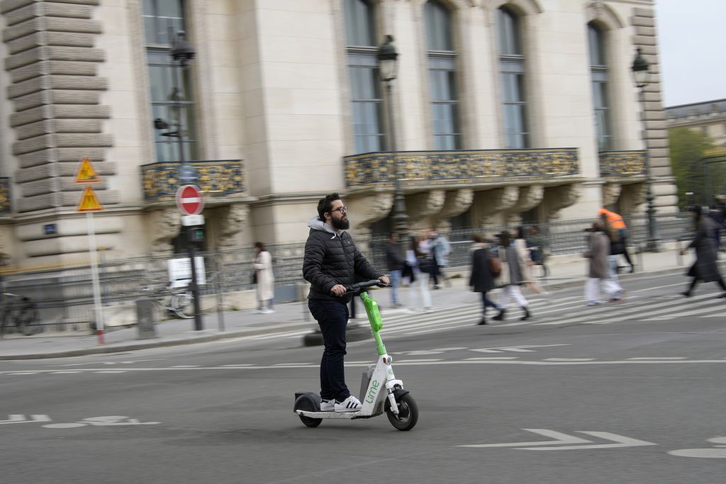 Seorang pengguna e-skuter sewaan tengah berjalan-jalan di sekitar Menara Eiffel di Kota Paris, Perancis, Jumat (31/3/2024). Mulai 1 September 2023, skutik sewaan dilarang beroperasi di Paris. (AP Photo/Christophe Ena)