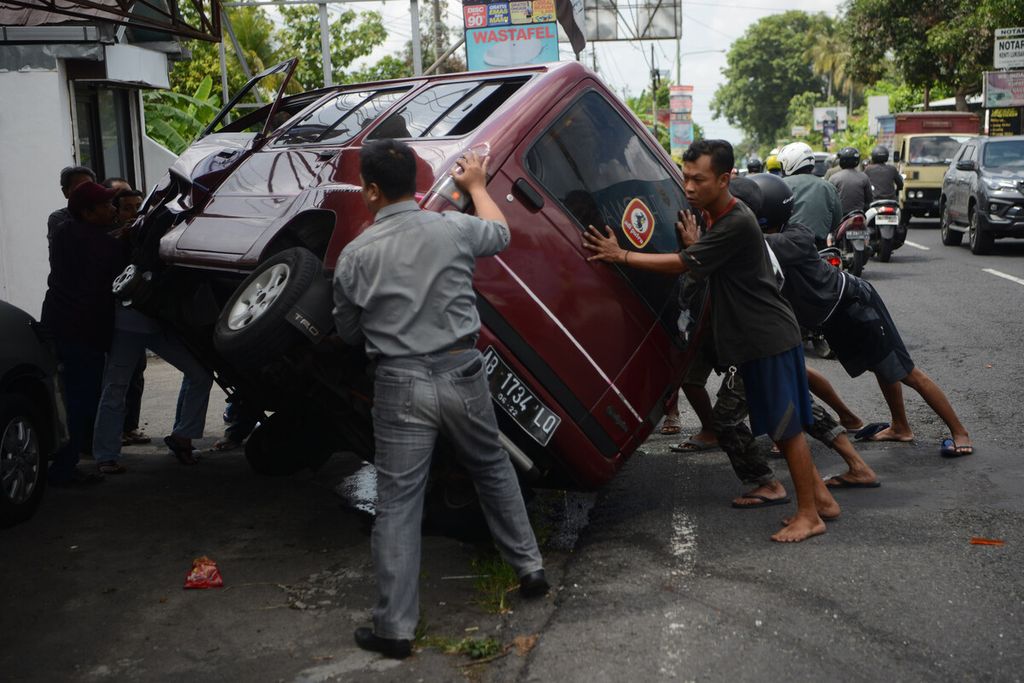 Warga membantu mendirikan sebuah mobil yang terguling setelah menabrak tiang listrik di Jalan Kaliurang, Sleman, DI Yogyakarta, Rabu (11/12/2019). Tidak ada korban jiwa dalam peristiwa tersebut.