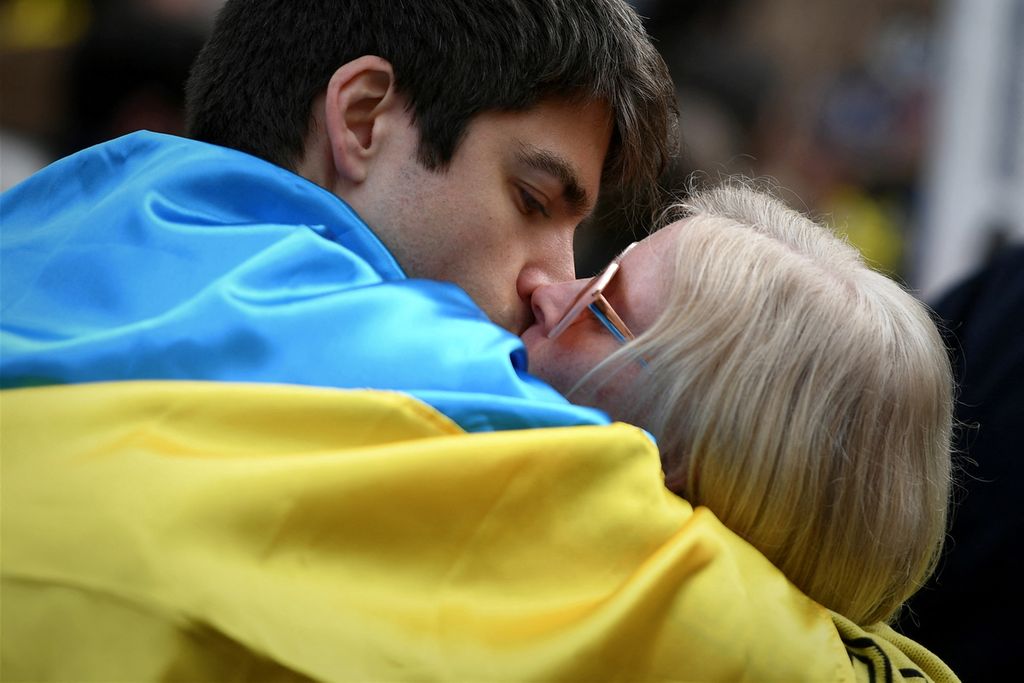 Sepasang kekasih, berbalut bendera nasional Ukraina, berciuman pada demonstrasi menentang invasi Rusia di Ukraina, di Toulouse, Perancis, pertengahan Maret 2022.