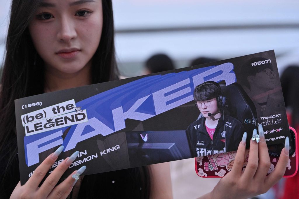 Seorang penggemar menunjukkan <i>merchandise</i> dari megabintang e-sport asal Korea Selatan, Lee Sang-hyeok, atau yang dikenal sebagai Faker, saat final League of Legends Asian Games 2022 pada 29 September 2023. Anak muda menjadi motor e-sport kian populer.